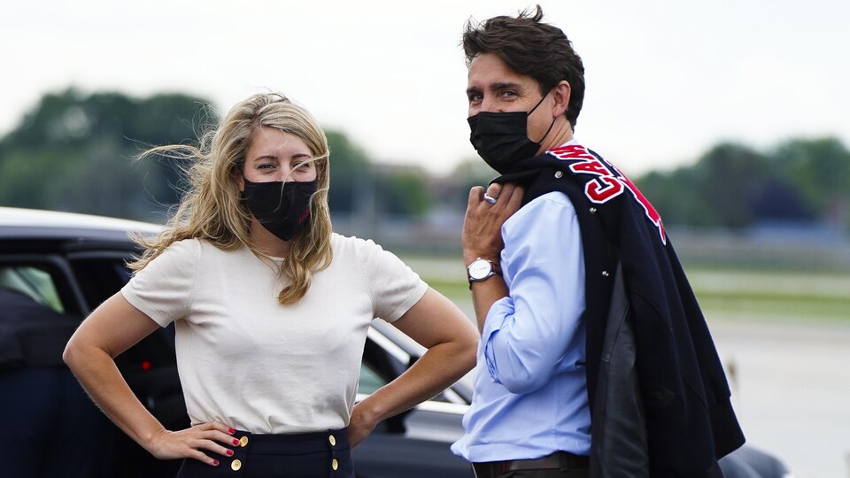 Les deux politiciens sont placés devant une voiture et regardent la caméra.
