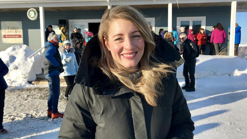 La ministre du Tourisme, Mélanie Joly, pose devant une caméra. Elle se trouve à l'extérieur d'un bâtiment en plein hiver. Elle porte un manteau isolé.