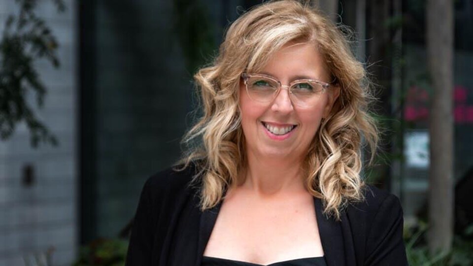 Une femme blondle avec lunettes qui sourit à la caméra