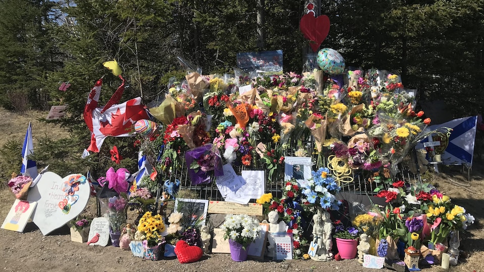 Un imposant mémorial rempli de fleurs, de ballons, de drapeaux et de messages de condoléances installés au bord d'une route.