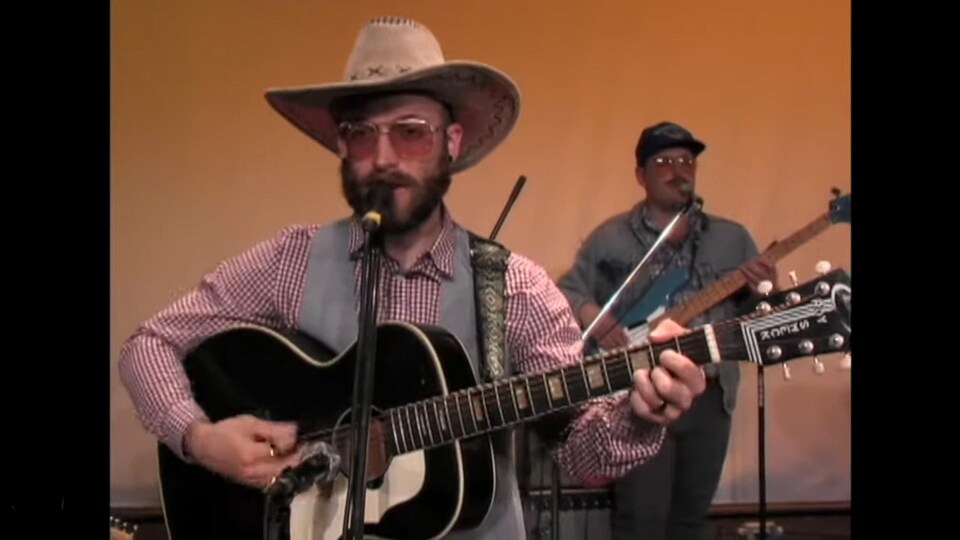 Une capture d'écran du nouveau vidéo-clip de Menoncle Jason. Il chante en grattant sa guitare.