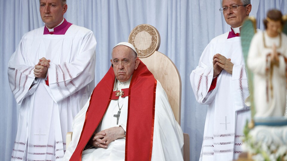Le pape François, assis, entouré de deux concélébrants 