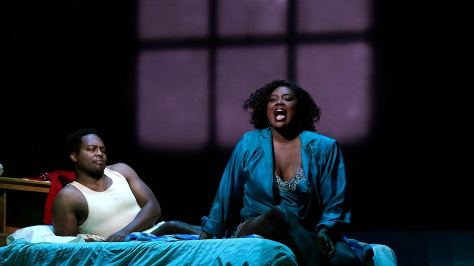 Les deux sont sur un lit. La femme chante.