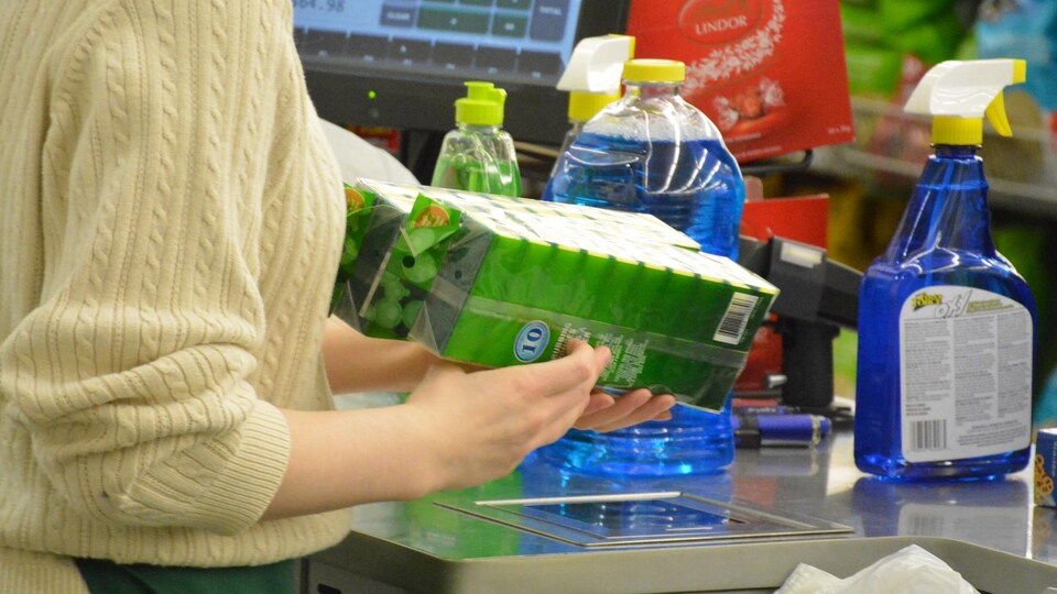Une travailleuse à une caisse enregistre les achats de consommateurs.