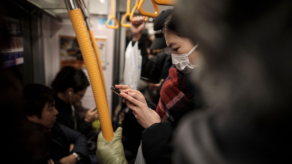 Une femme masquée regarde son téléphone dans un wagon bondé.