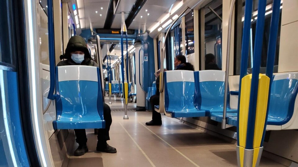 Deux personnes, dont une masquée, sont assises à bonne distance dans un wagon de métro vide.