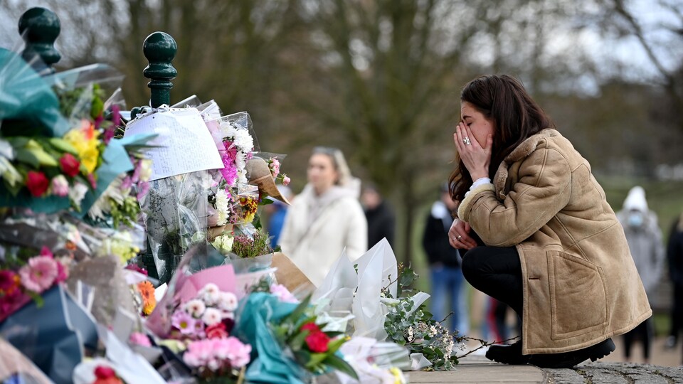 Une femme accroupie se recueille devant les fleurs.