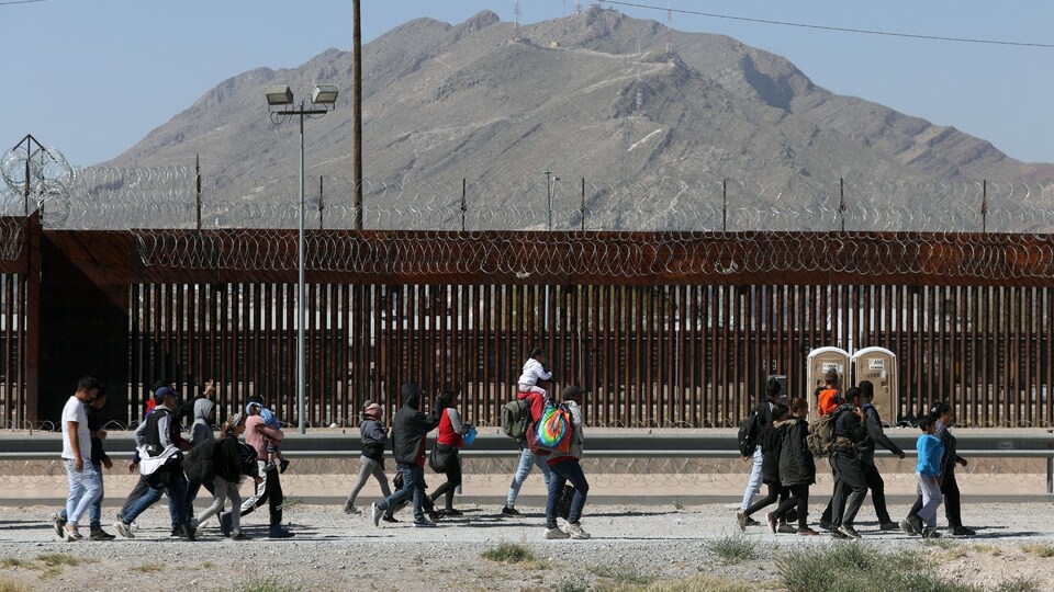 Un groupe d'hommes, de femmes et d'enfants marchent près d'une clôture.