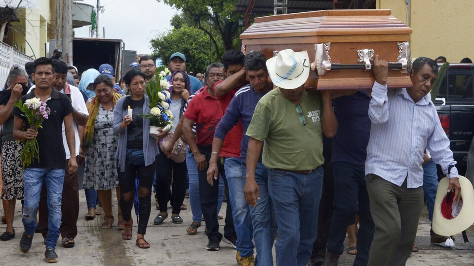 Une procession derrière un cercueil de bois porté par des hommes.