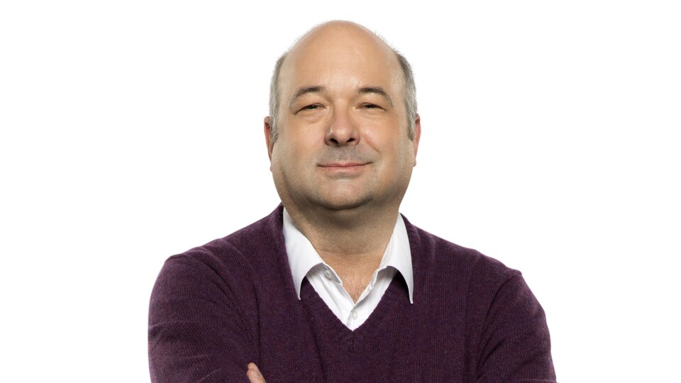 Michel C. Auger sourit légèrement en ayant les bras croisés.