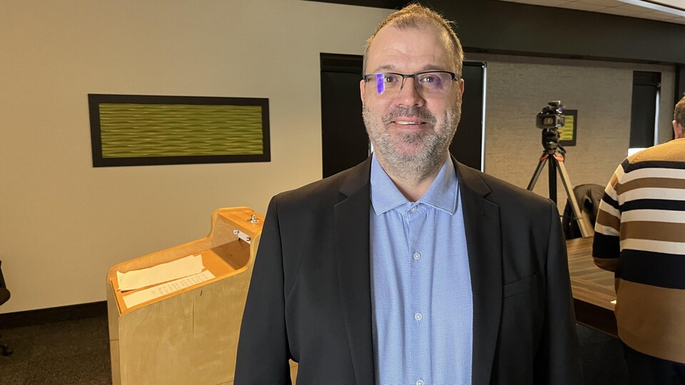 Michel Desbiens sourit à la caméra dans une salle de conférence.