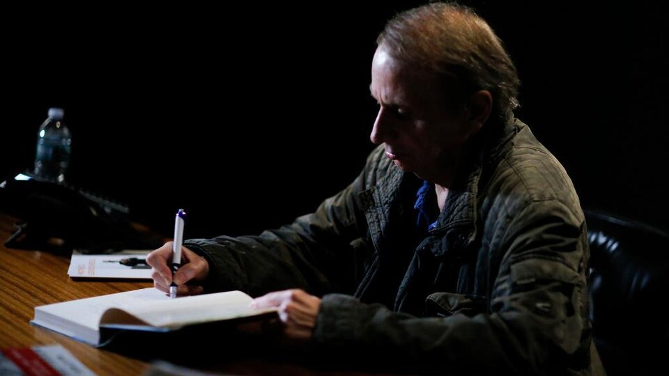 L'écrivain Michel Houellebecq signant un livre sur une table.