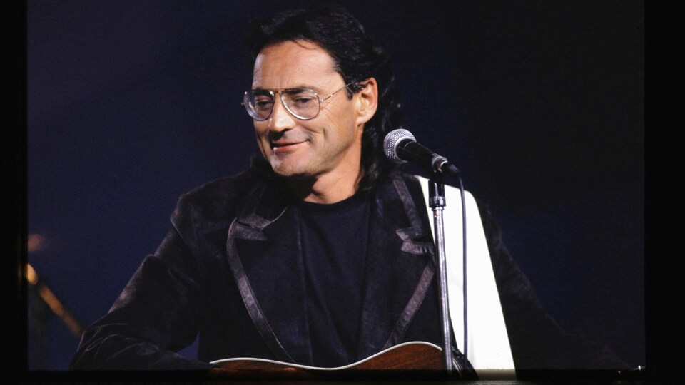 Le musicien est sur scène et sourit devant un micro.