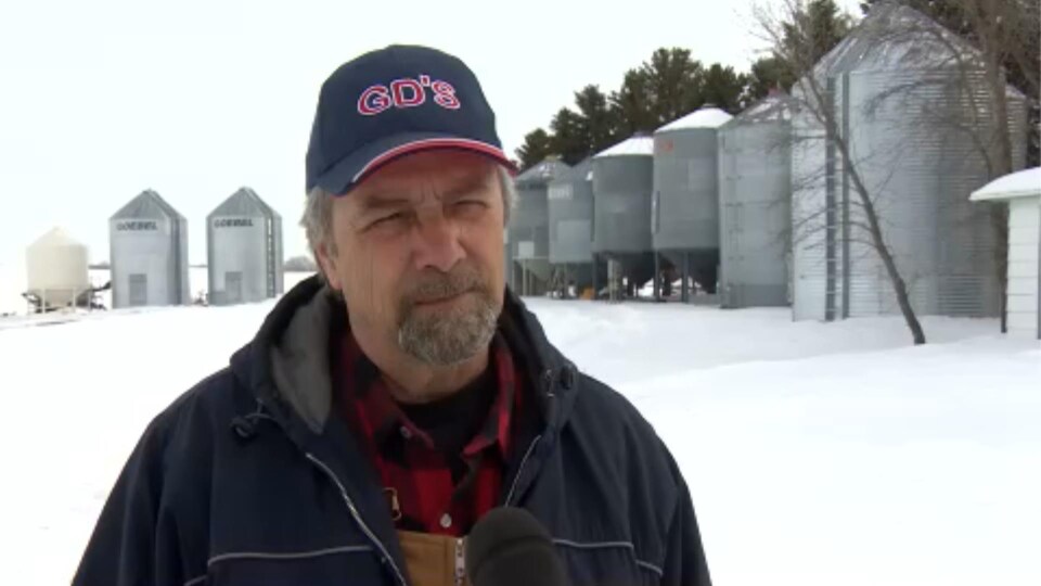 Michel Lepage donne une entrevue en plein air sur sa ferme, en arrière-plan se dressent plusieurs silos.