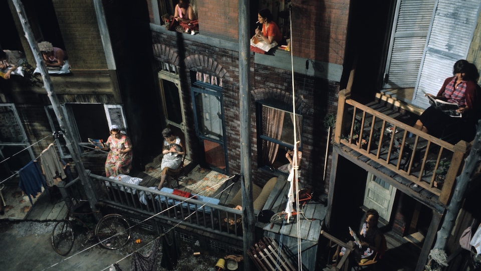 Un décor de théâtre évoque une ruelle du Plateau-Mont-Royal avec des femmes sur le bord de leurs fenêtres ou de leurs balcons.