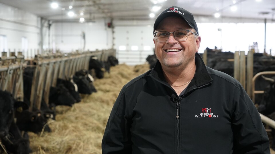 Un homme souriant devant son troupeau de bœuf Wagyu dans son étable.