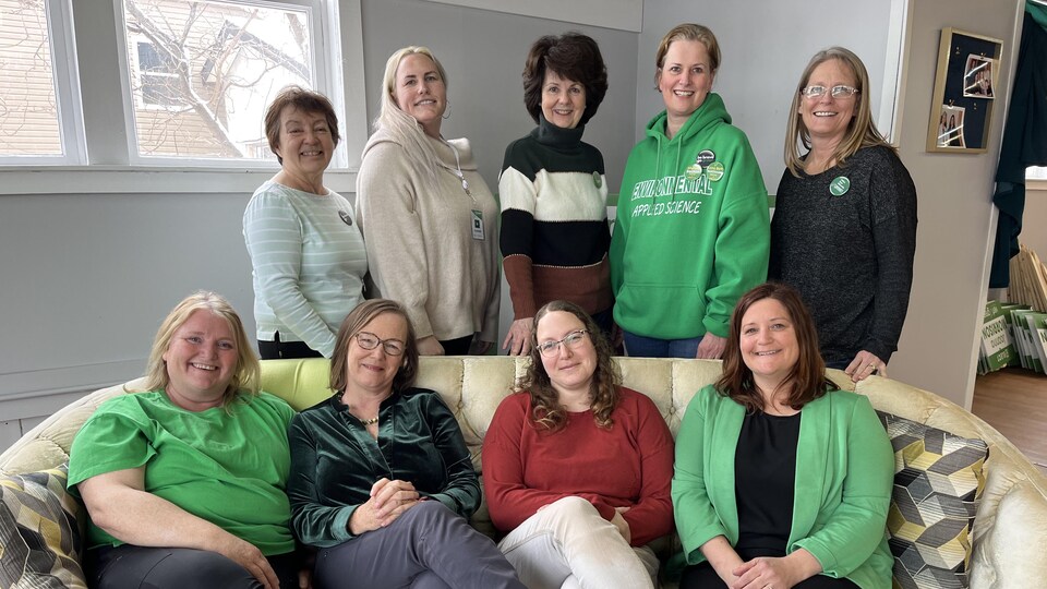 Quatre femmes sont assises sur un canapé, cinq autres sont debout. Toutes posent pour la photo. 