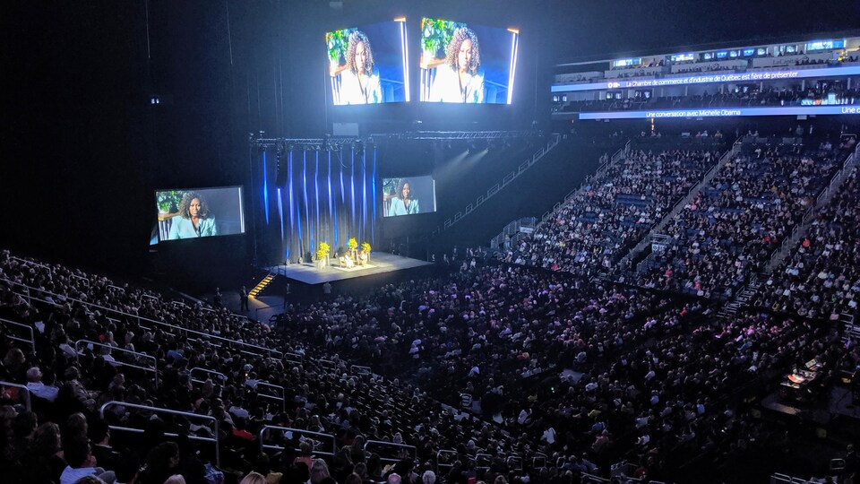 Une salle de spectacle avec un large public ainsi qu'une scène sur laquelle on voit Michelle Obama.