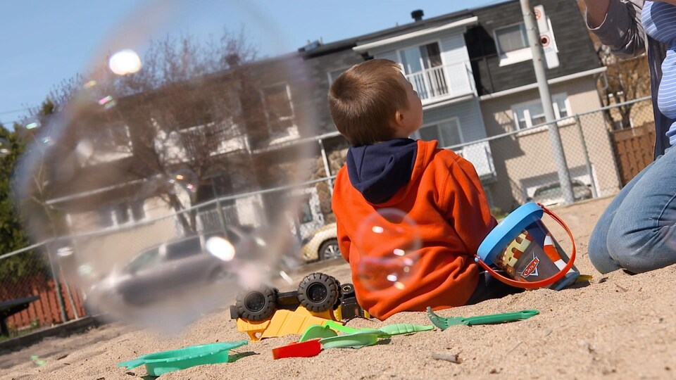 L'enfant est assis dans le sable, entouré de ses jouets.