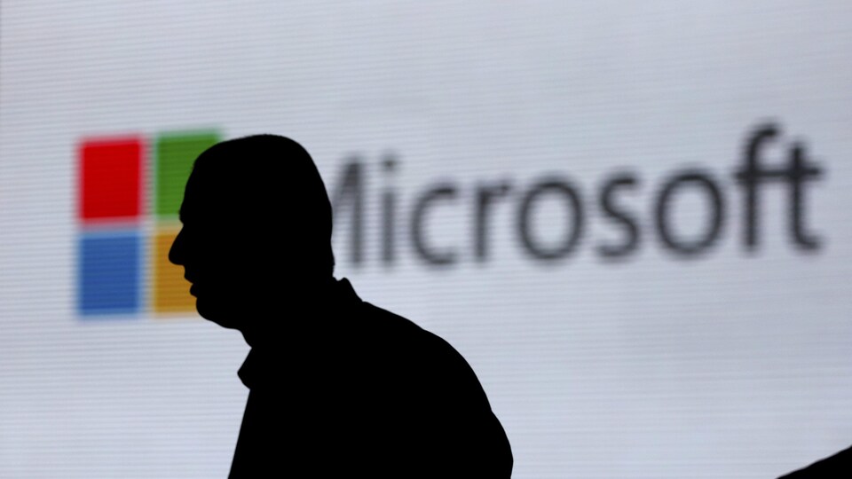 La silhouette d'un homme se dessine sur un écran où est projeté le logo de Microsoft.