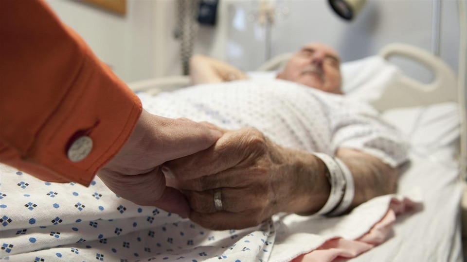 Un patient alité dans une chambre d'hôpital tient la main d'une autre personne.