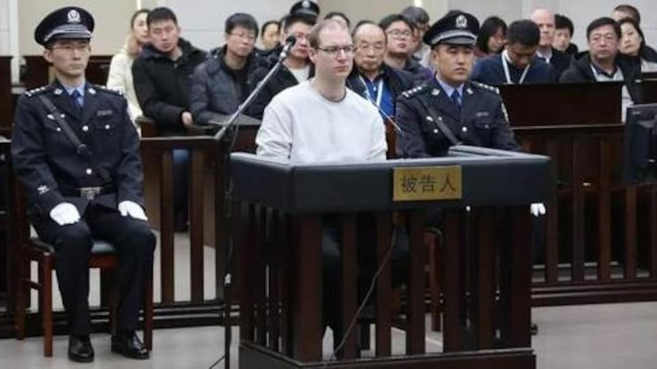 Le Canadien Robert Lloyd Schellenberg est assis dans le box des accusés flanqué de deux policiers chinois.