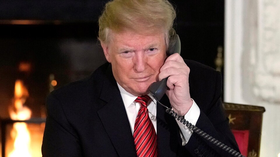 M. Trump est au téléphone; il y a derrière lui un foyer et un sapin de Noël.