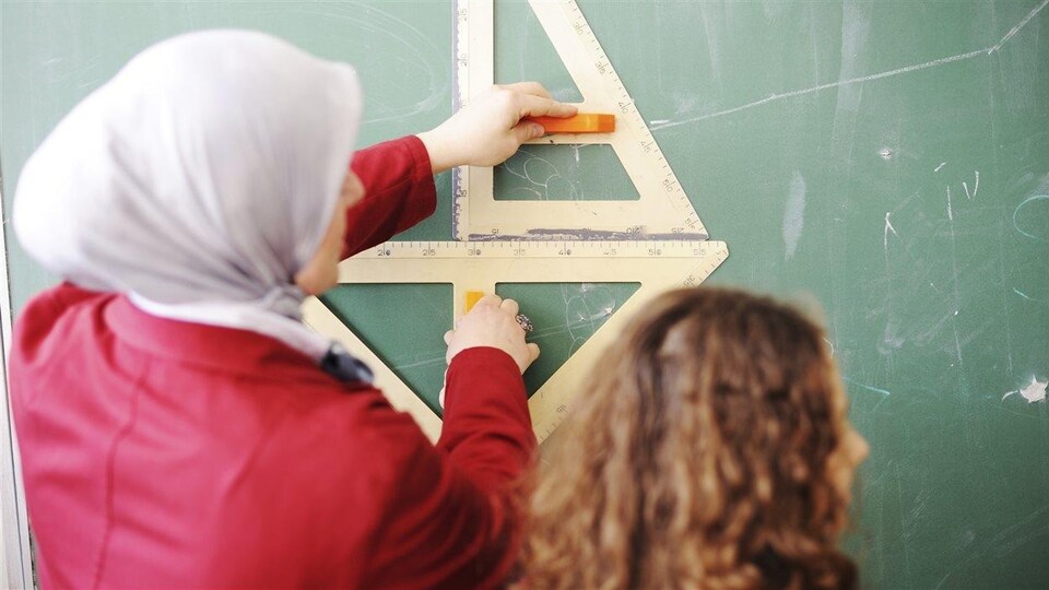 Une enseignante arborant un voile donne des explications à une élève.