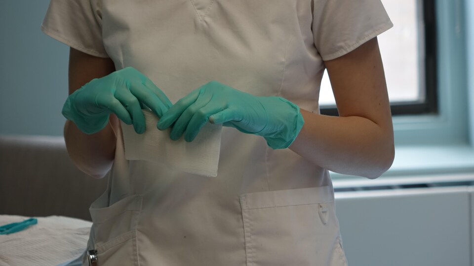 Les mains d'une infirmière, avec des gants verts, qui tient de la gaze.