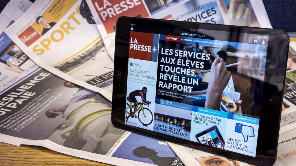 La version numérique de La Presse (La Presse +) sur une tablette en avant-plan et plusieurs cahiers du journal La Presse sous forme papier en arrière-plan