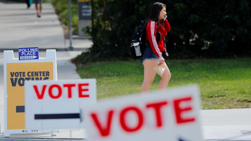 Une étudiante parle au téléphone alors qu'elle marche près de pancartes indiquant aux étudiants où aller voter à l'Université d'Irvine, en Californie.