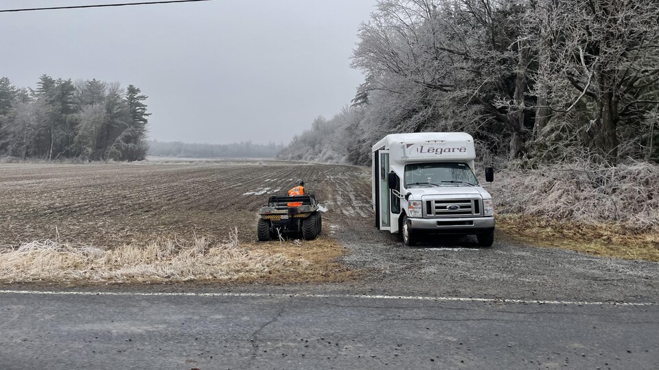 Two vehicles are parked near a field and wooded area.