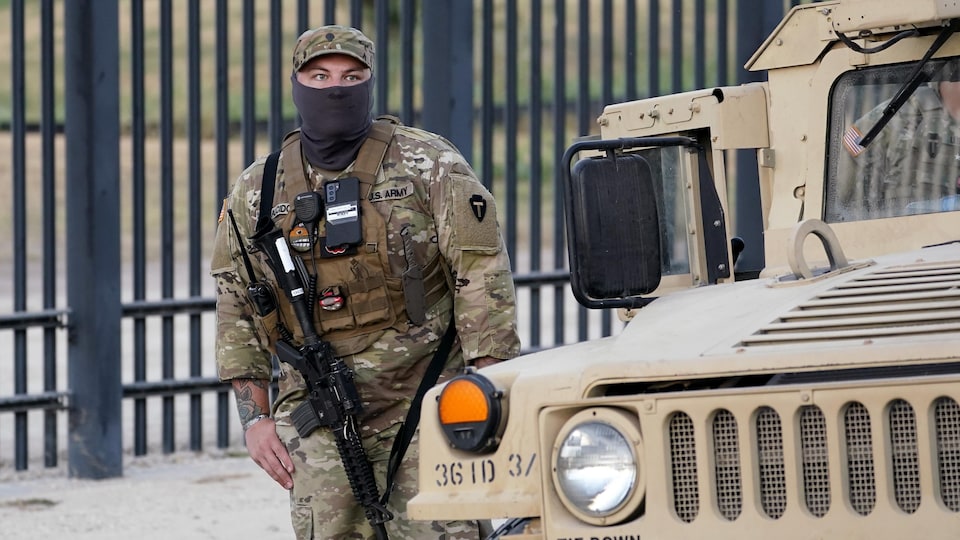 Um soldado americano armado com um rifle de assalto está perto de um carro.