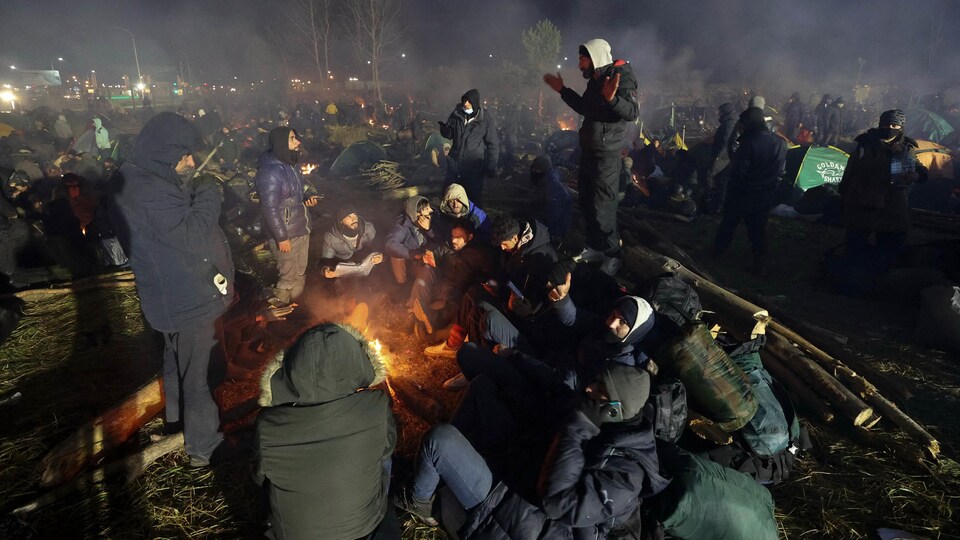 La nuit, des migrants se réchauffent près d'un feu dans un camp à la frontière.