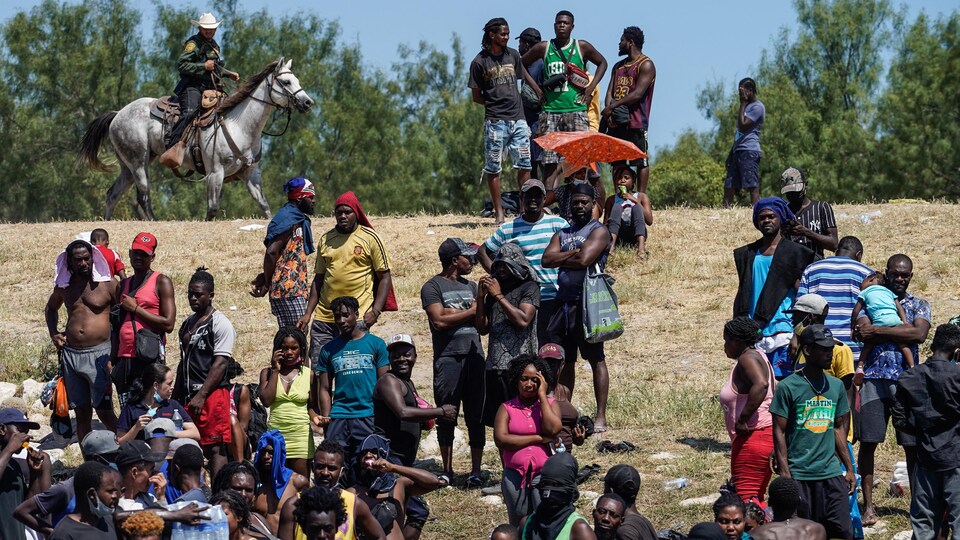 Des Haïtiens sur la rive du Rio Grande, surveillés par un policier à cheval.