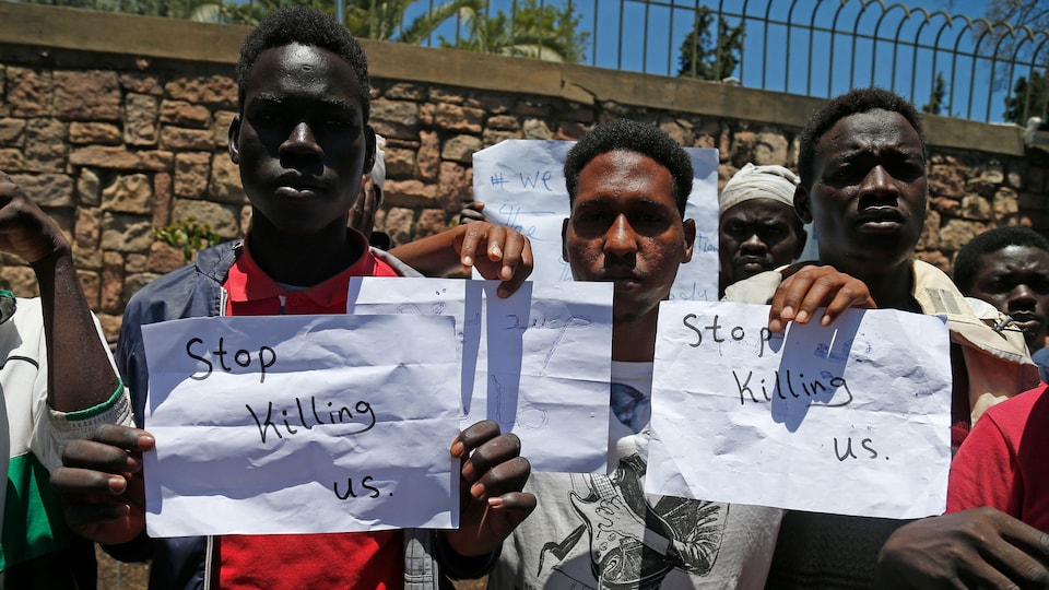 Des migrants tiennent des pancartes, où il est écrit « stop killing us » (arrêtez de nous tuer). 