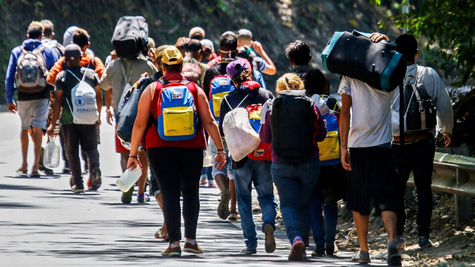 Une vingtaine de personnes de dos marchent sur le bitume avec leurs sacs sur le dos.