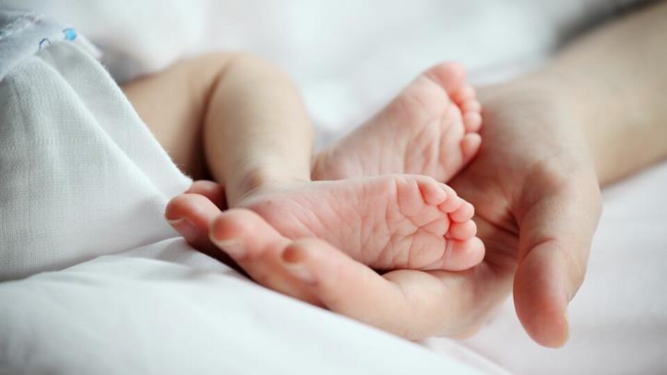 Des pieds de bébé sur une main d'adulte.