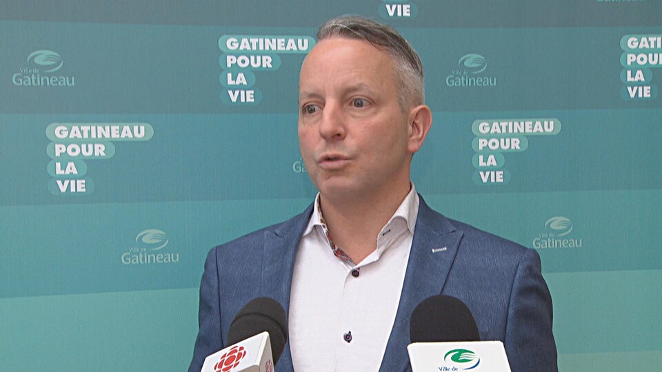 Mike Duggan s'adresse aux médias devant une bannière comportant le logo de la Ville de Gatineau.