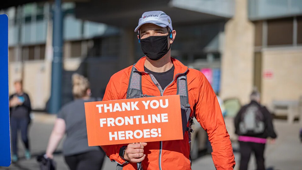 Le coureur tient dans sa main un affiche sur laquelle il est écrit, en anglais, « Merci aux travailleurs de première ligne, des héros ».