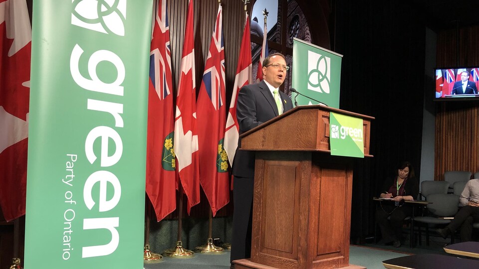 Un homme en complet se tient derrière un podium entouré de bannières vertes du Parti vert