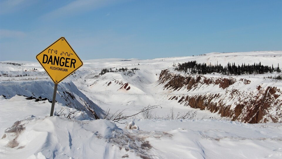 Vue sur un trou de mine enneigé avec un panneau « danger » traduit en innu et en naskapi.