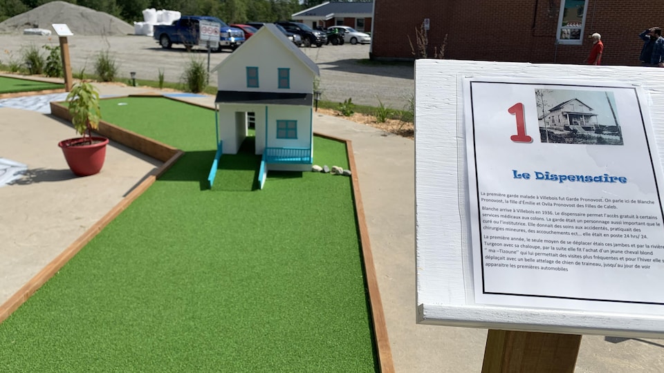 Une petite maison est posée près d'un trou de mini-golf. Une description du Dispensaire qui « permettait l'accès gratuit à certains services médicaux aux colons » est tout près.