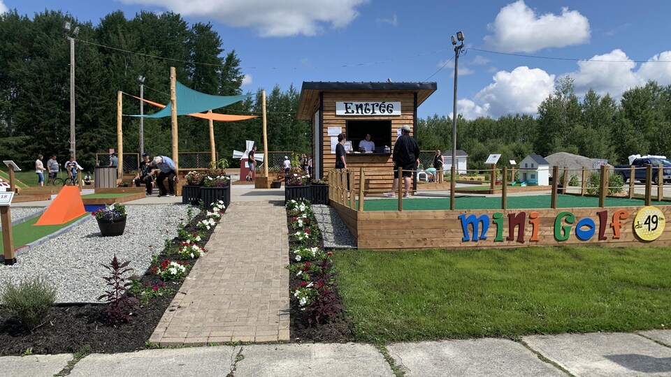 Des personnes attendent à l'accueil du mini-golf pendant que d'autres tentent de faire entrer la balle un des 18 trous.