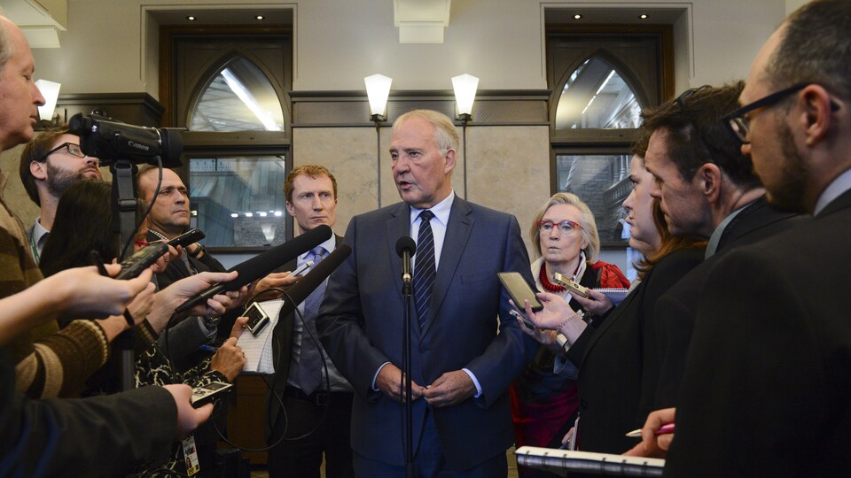 Trois ministres fédéraux, deux hommes et une femme, se tiennent devant des journalistes. Des micros et des caméras sont pointés vers eux.
