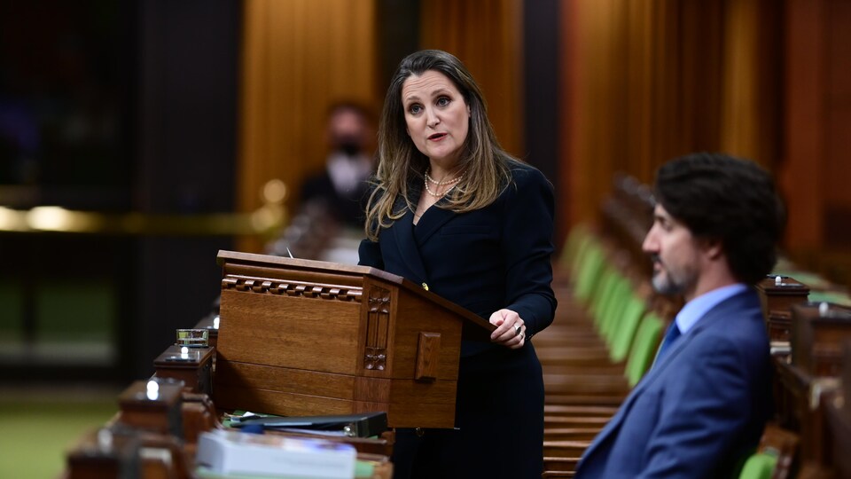 Chrystia Freeland parle au lutrin aux Communes, pendant que Justin Trudeau l'écoute, assis.