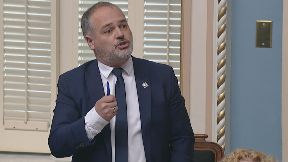 Le ministre Jonatan Julien est debout à l'Assemblée nationale et il répond à une question.