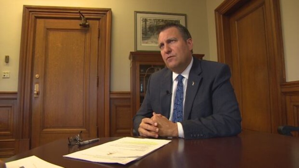 Le ministre assis sur une table avec des documents devant lui.