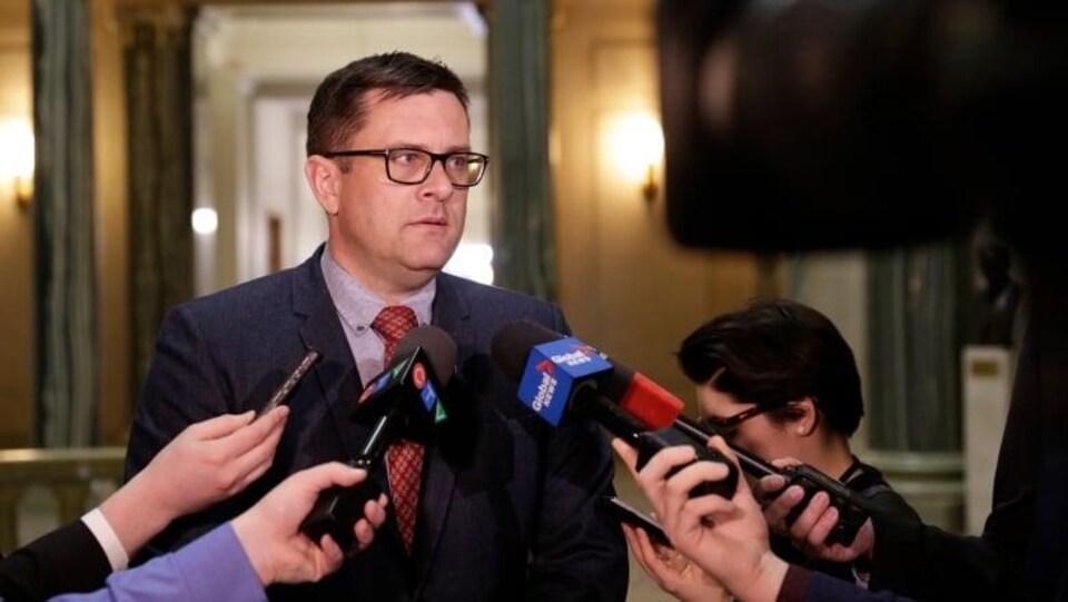 Le ministre Paul Merriman debout donne une entrevue à des journalistes. (archives)