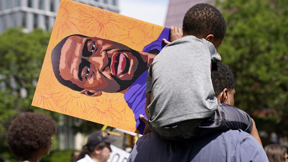 À Minneapolis, un enfant sur les épaules de son père avec une pancarte représentant George Floyd.
